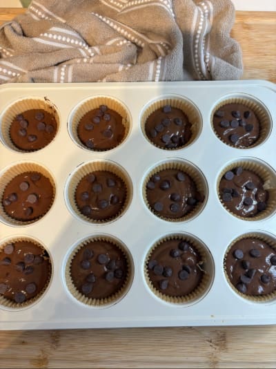 Paper-lined muffin tray with chocolate batter and chips