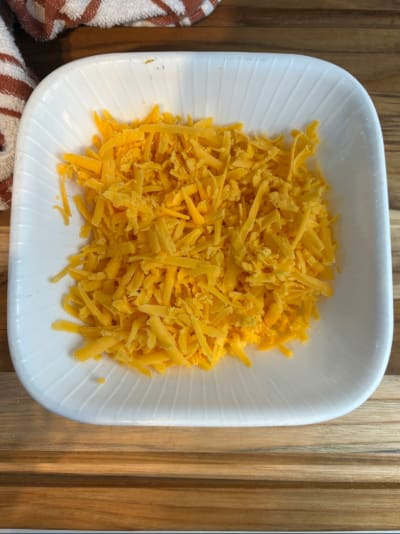 Shredded cheddar cheese in white bowl